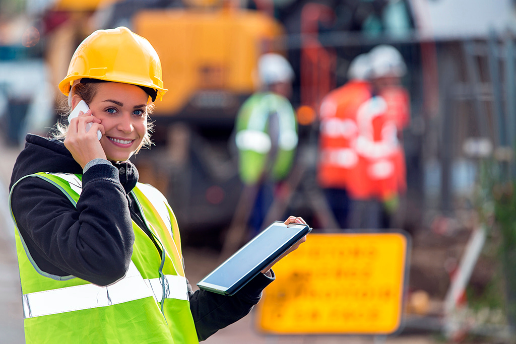 female field worker in high vis hard hat on mobile using tablet ipad