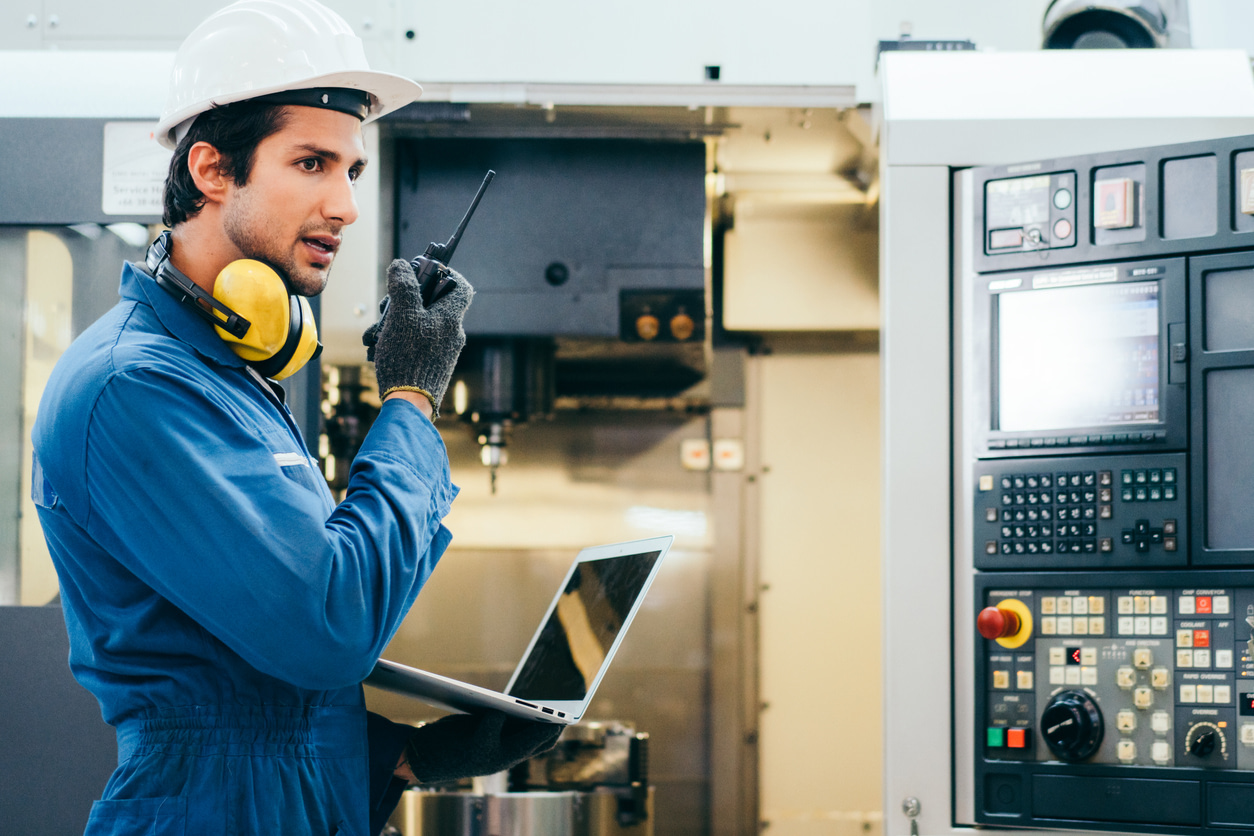 Male engineer conducting preventive maintenance, talking thru a radio phone while holding a laptop.